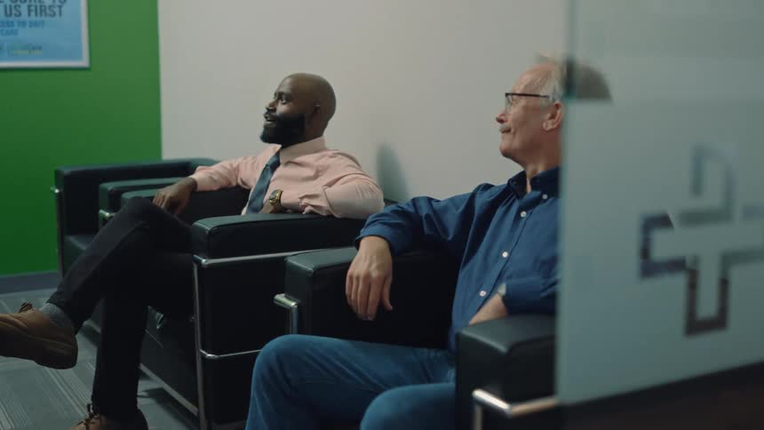An elderly man and a black man sitting in a waiting area