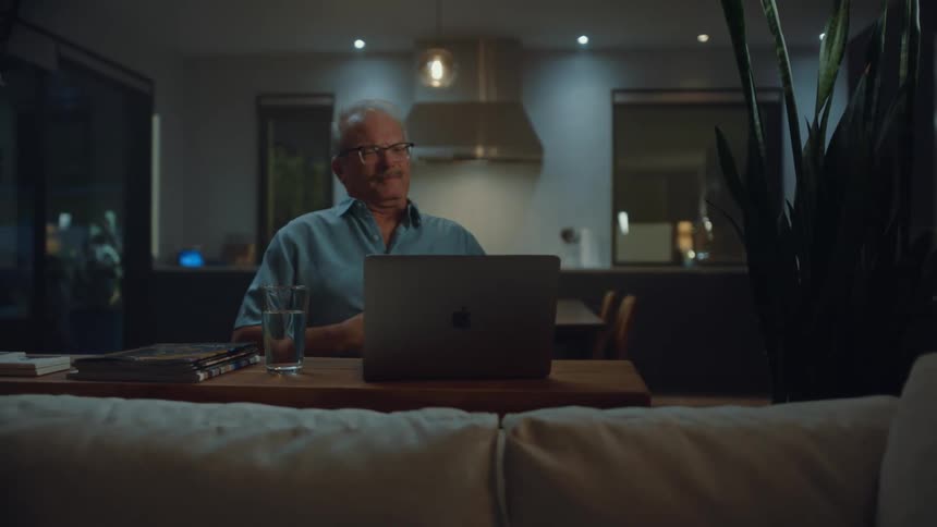 An adult man is sitting indoors at a table using a laptop