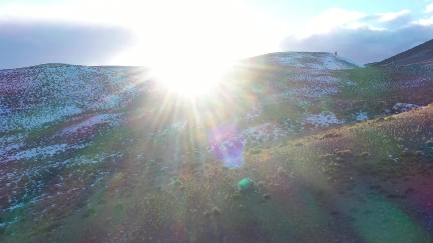 A bright sun shines over snowdusted hills in a wide open natural landscape