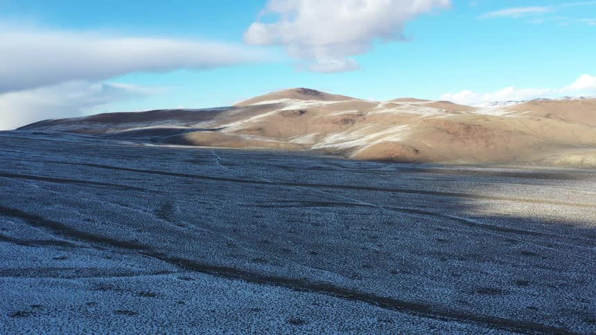 A wide aerial shot captures a barren snowdusted highland landscape under a bright blue sky