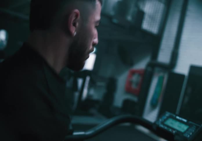 A man intensely runs on a curved treadmill in a dimly lit gym