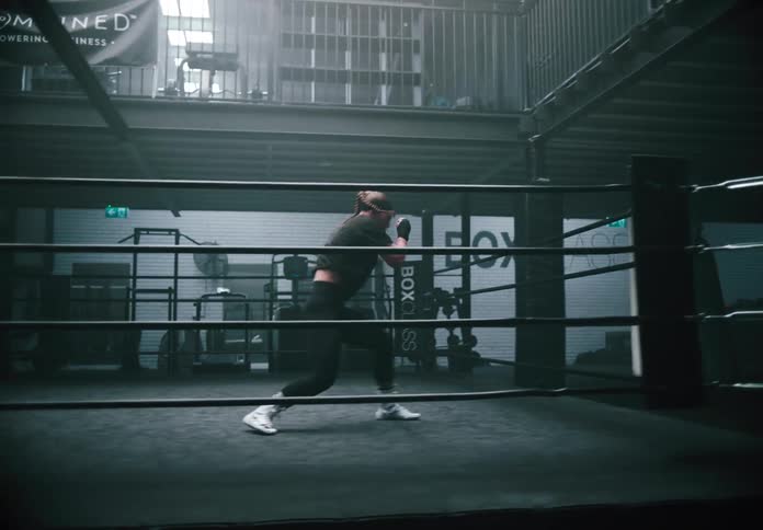 A young woman is alone in a boxing ring shadow boxing