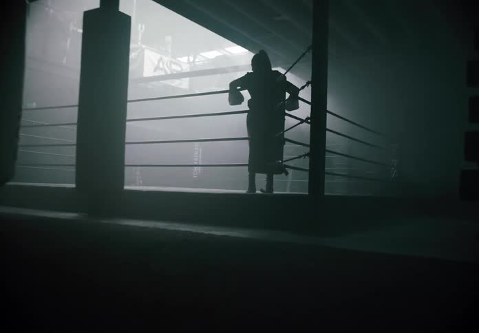 Female boxer standing in the corner of a boxing ring is silhouetted by the light