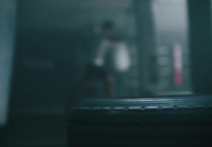 Hammer hits a tire in a boxing gym while a boxer trains in the background