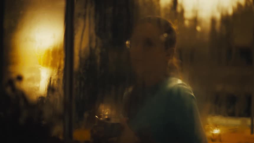 A woman is seen blurred through a steamy window drinking and staring outside
