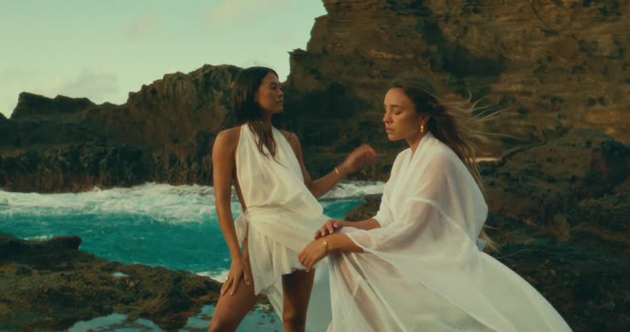 Two models pose together on the rocks of the shore