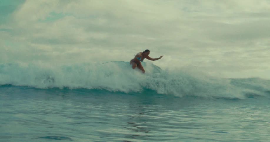 A person surfs a wave in the ocean under a cloudy sky