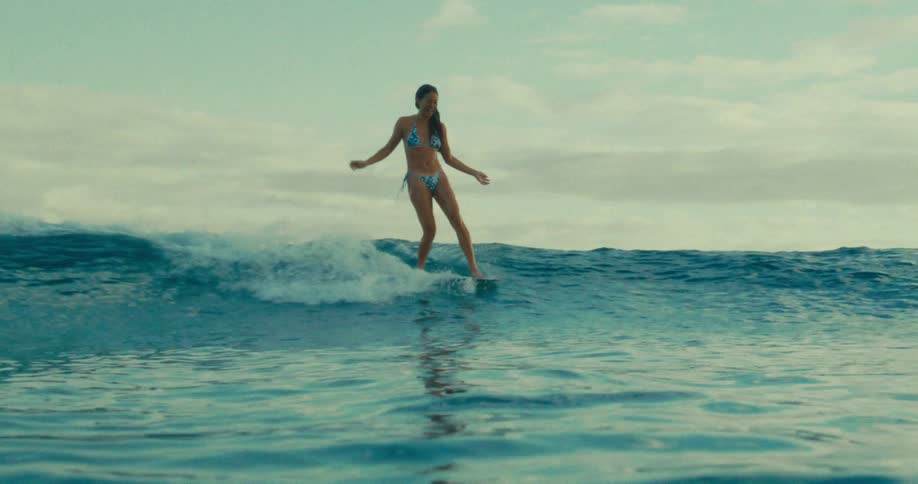 A woman surfing a wave in the ocean wearing a bikini