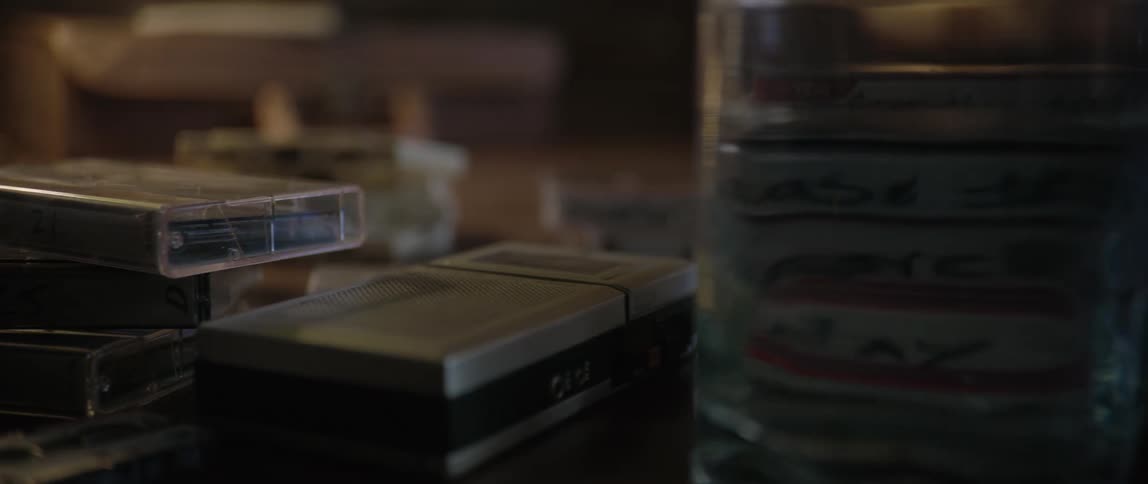 A series of tapes and cassettes are placed on a desk alongside a glass of water