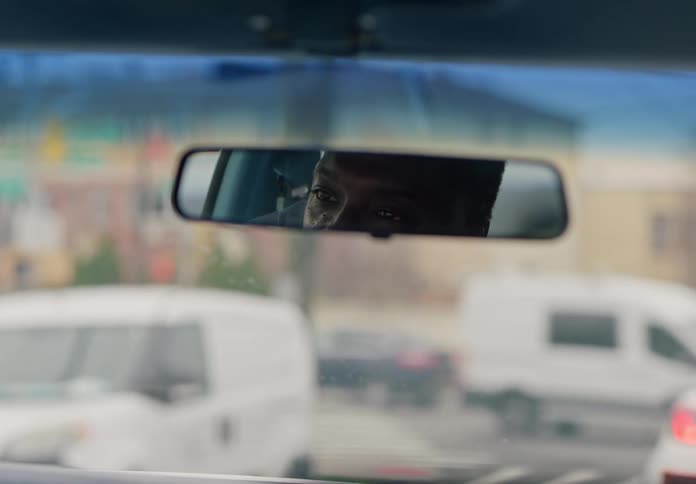 A mans eyes are seen through a cars rearview mirror as he drives through a city