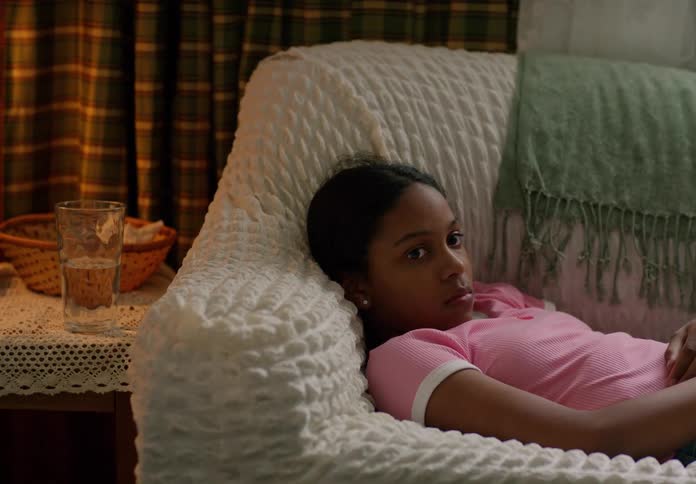 A young girl is lying on a couch staring thoughtfully ahead in a calm living room setting