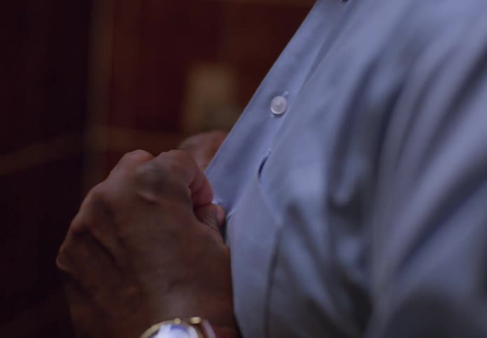 A man wearing a watch is buttoning his dress shirt