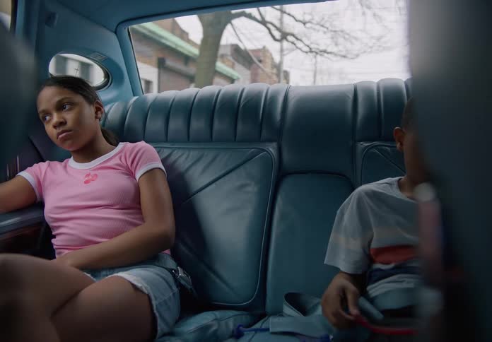 A little boy in a car plays with a toy while his older sister looks bored