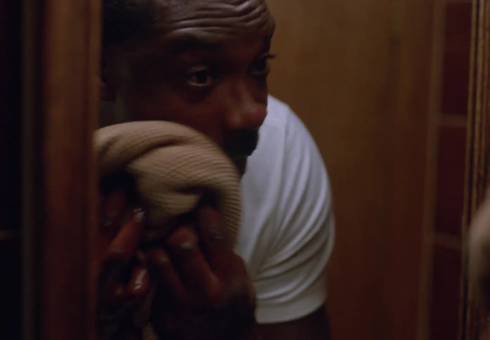 A man in a bathroom drying his face in front of a mirror