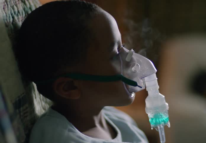 Boy receives a breathing treatment via a nebulizer while sitting in his living room