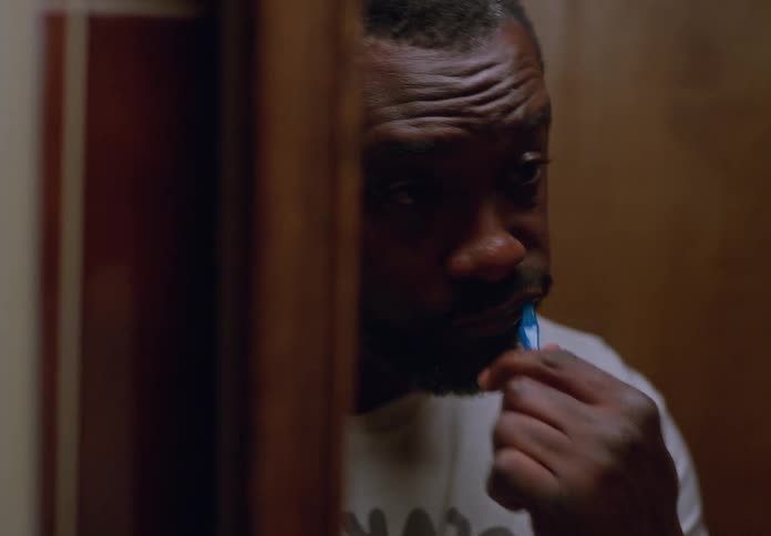 Man faces his reflection in the bathroom mirror while brushing his teeth