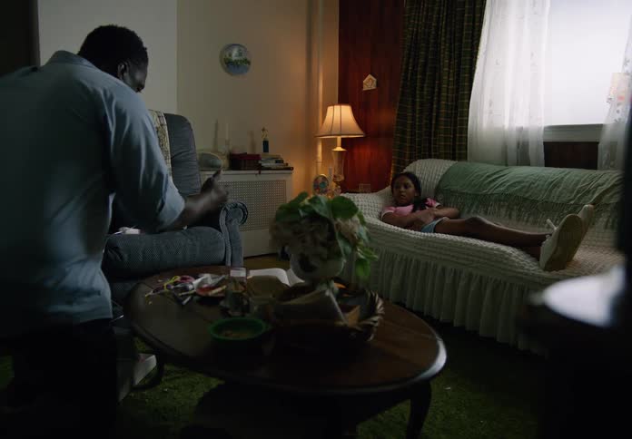 A young boy uses a nebulizer while a girl watches quietly in a dimly lit living room
