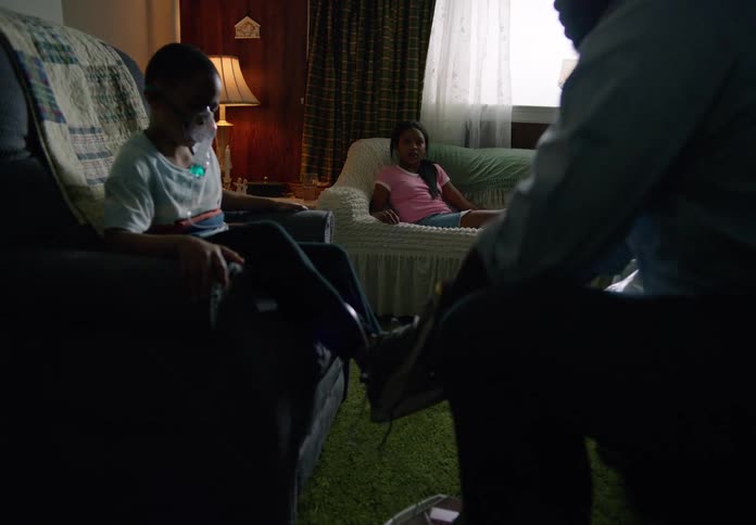 A man puts a shoe on a boy who is sitting with a nebulizer mask on his face