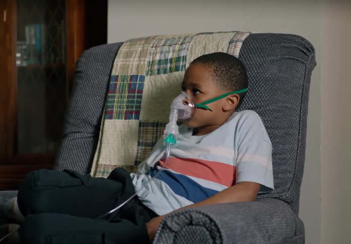 A boy uses a nebulizer quietly watching his dad on a call with the doctor