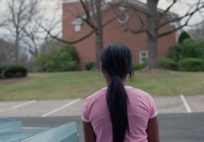 A young girl steps out of a vintage car looking upset as her family follows in a suburban neighborhood
