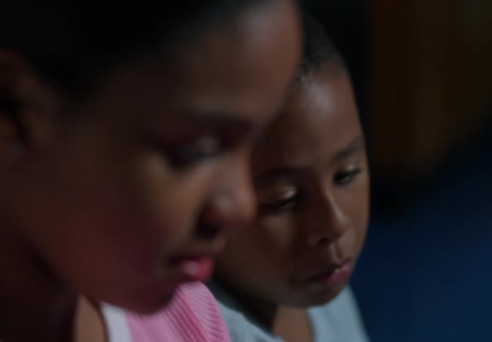 A young boy silently chews food while sitting next to his sister