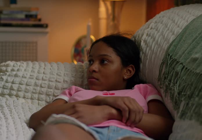 A young girl is lying on a couch looking off to the side with a thoughtful expression