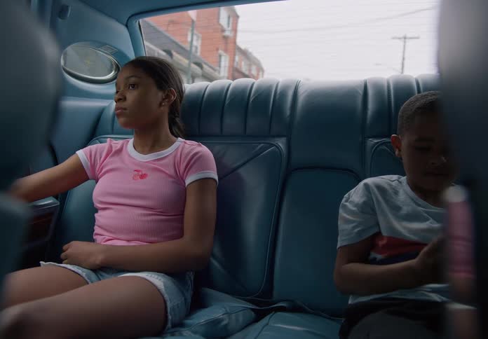 Two kids sit silently in the back seatone gazing out the window the other fiddling with something