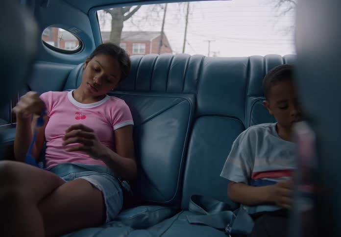 Two kids sit in the backseat of a blue car focused on playing with colorful strings