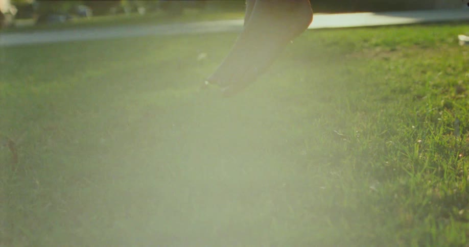 Bare feet of a child are gently suspended above a sunlit patch of grass