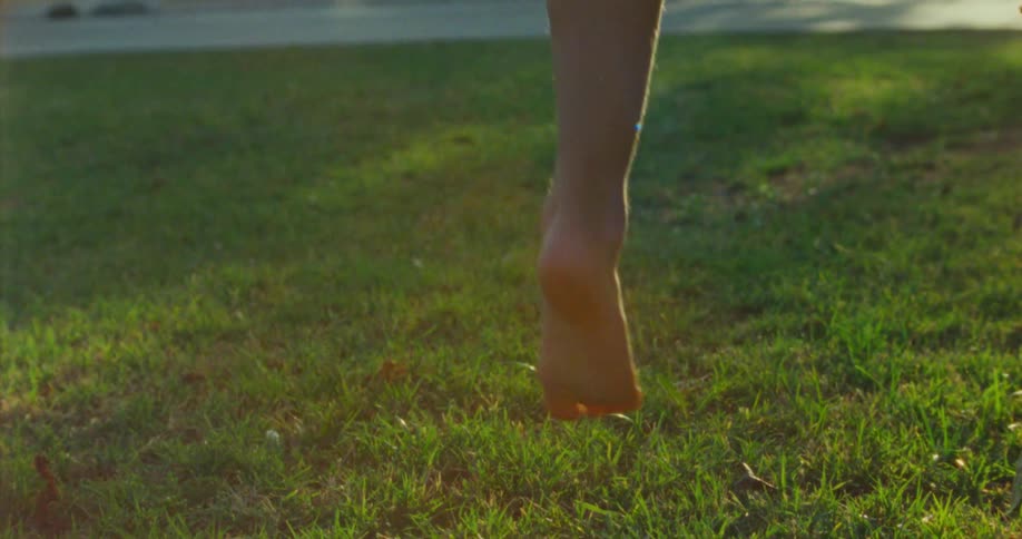 A person levitates in midair on a lawn at midday singing with their feet extended forward and backward