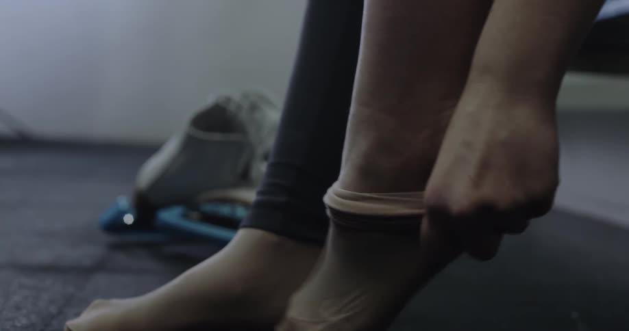 A girl puts stockings on her feet with ice skates on the floor nearby