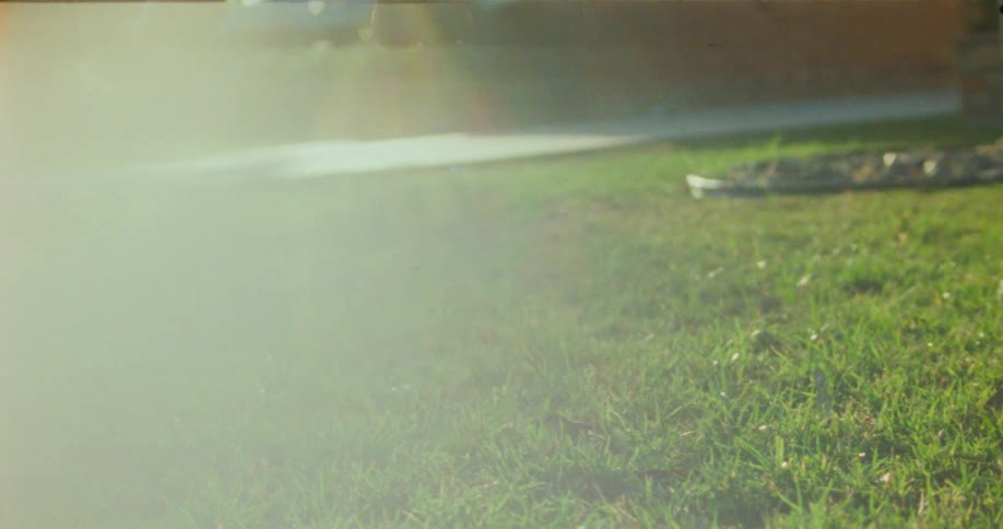 Bare feet dangle in the bright sunlight against a backdrop of trees a house and a lawn