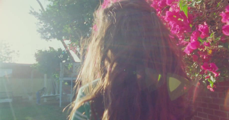 A young girl plays hide and seek beside a bright wall of blooming pink flowers in the sun