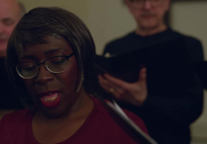 A small group of people are holding books and singing in a church choir