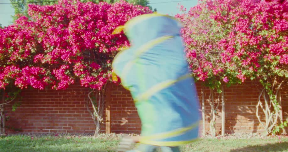 Two people wrapped in blankets run past two large pink bougainvillea plants