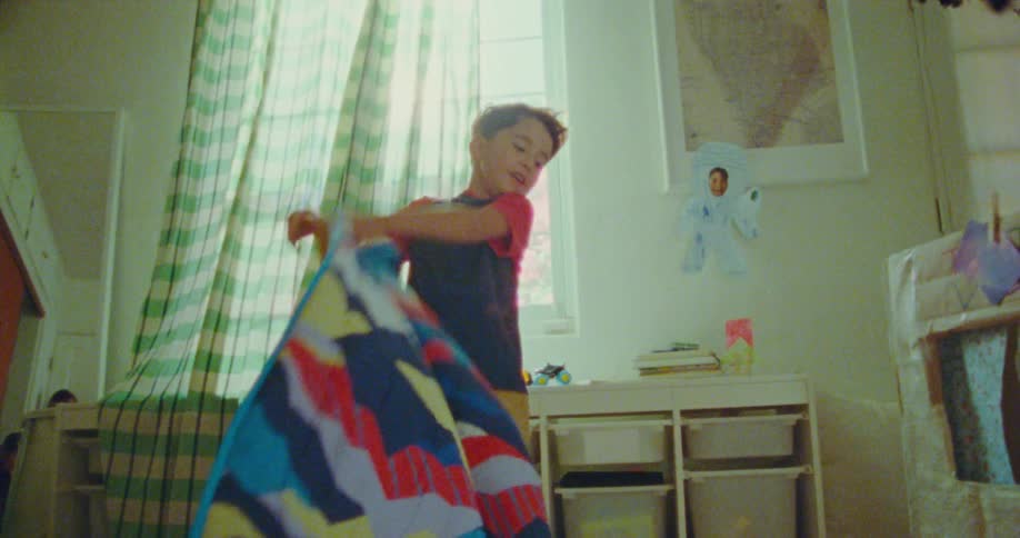 Two kids play in their bedroom at midday as the young boy lifts the blanket to reveal his sister hiding underneath