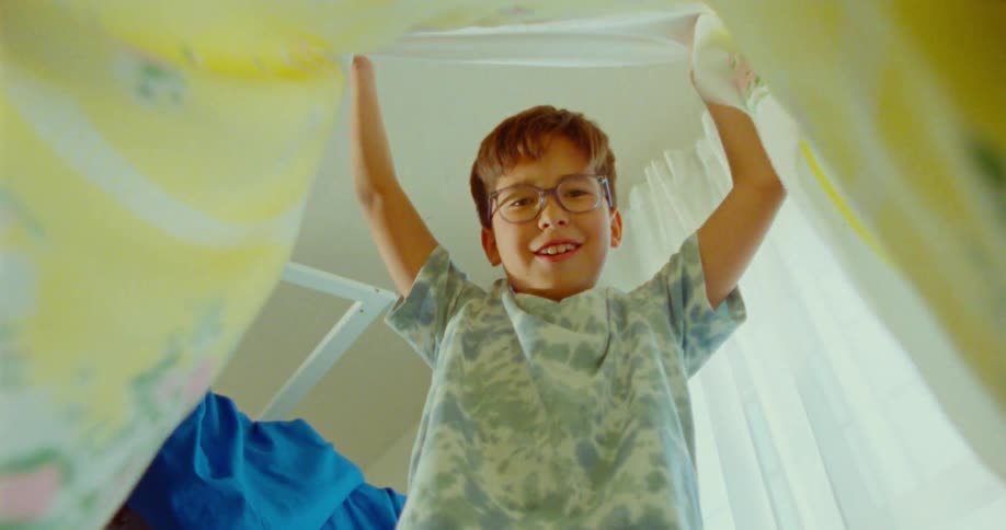 A child wearing glasses lifts up a blanket searching for other kids during a game of hide and seek