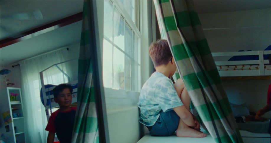 A kid hides behind a curtain next to a window at midday as another kid discovers the hiding spot during a game of hide and seek