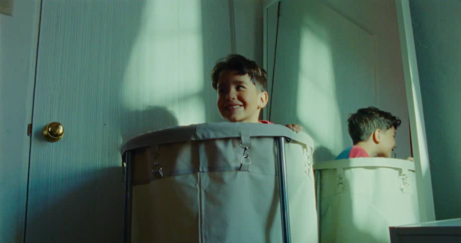 A child hides inside a laundry basket next to a mirror filled with excitement during a game of hide and seek