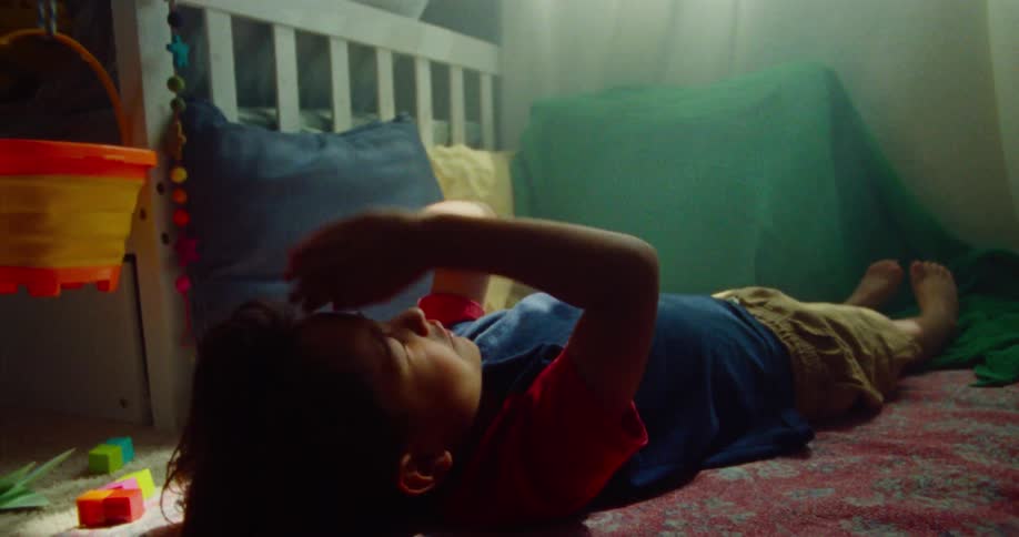 A playful young boy lies indoors on the floor eyes shut then opens them looking up