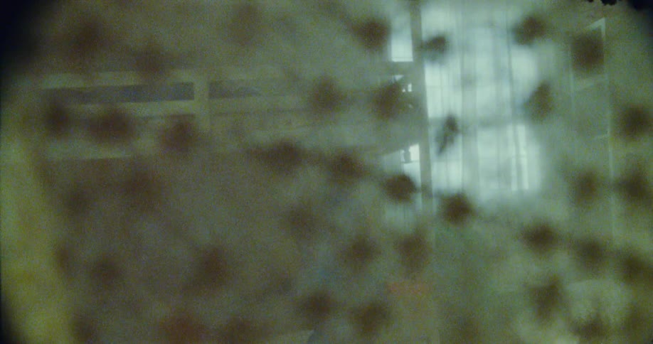 A child playing hide and seek wearing glasses walks near a window partially visible through a textured and outoffocus foreground