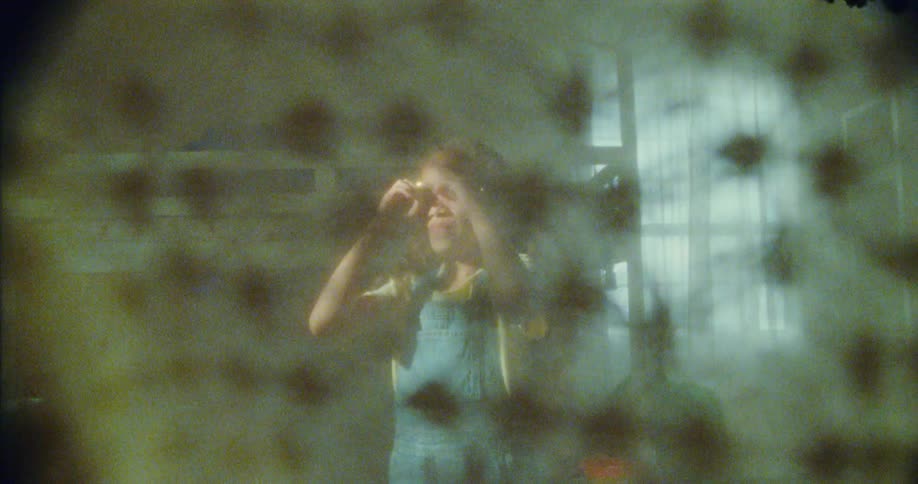 A girl person wearing a yellow shirt and blue overalls is searching for other children playing hide and seek