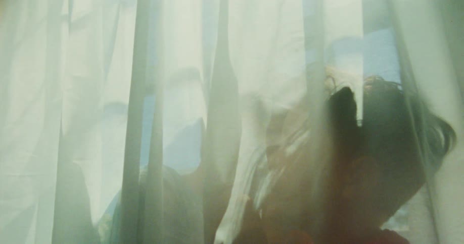 Two children play behind the curtains near a window on a sunny day whispering secrets to each other while wrapping themselves in the fabric and spinning