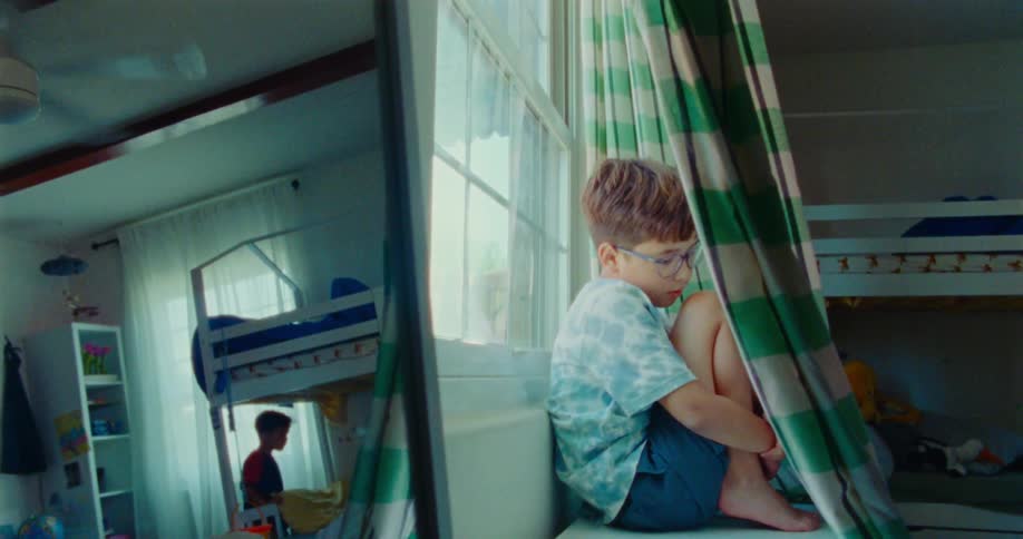 Boy making a silence sign while hiding behind a curtain and another child reflected in a mirror is looking