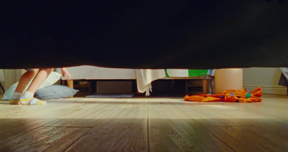 A young boy tiptoes around as he looks under furniture for someone