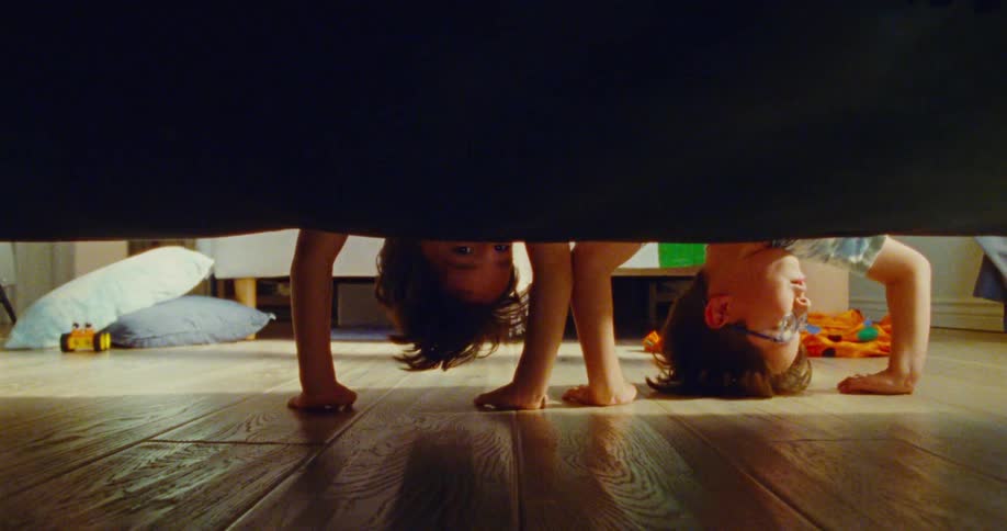Two children curiously look under a couch while playing on the floor