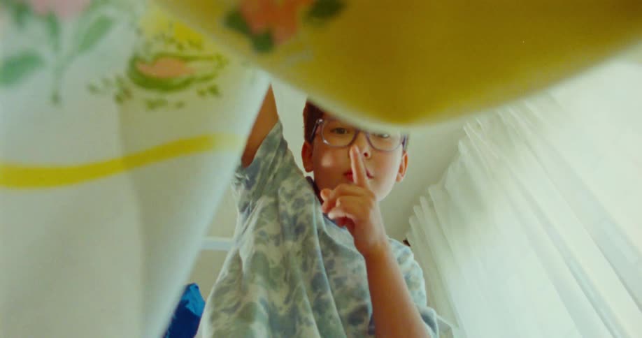 A boy puts his finger to his lips and drops the blanket
