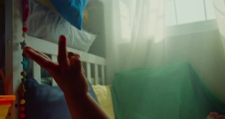 A child lies on their back on a patterned floor near colorful toys and a blue beanbag chair with his arms raised