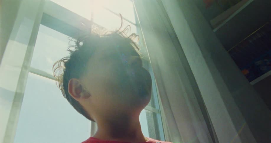 A young boy playfully peeks out from behind a curtain with a bright happy smile