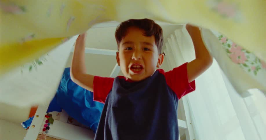Young boy lifts a blanket playfully looking down